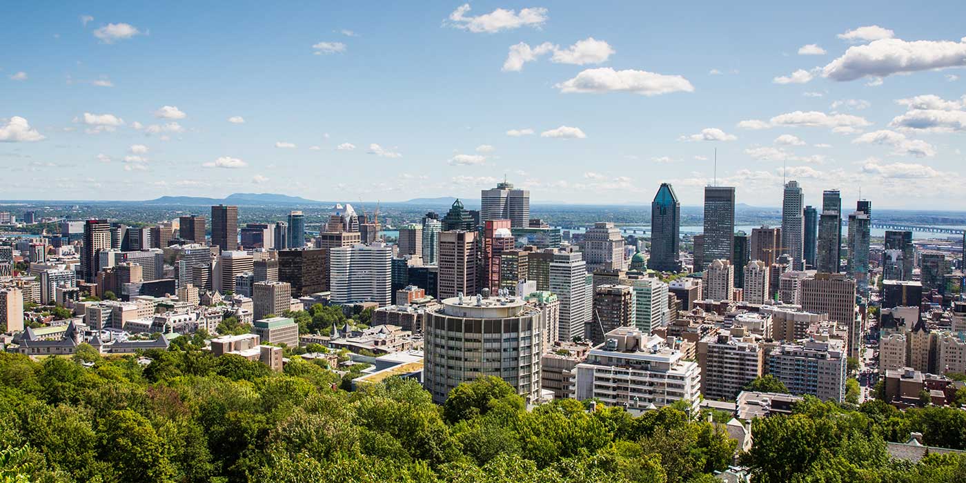 A vibrant city skyline featuring a mix of modern skyscrapers and historic buildings under a clear blue sky with scattered clouds, surrounded by lush greenery.